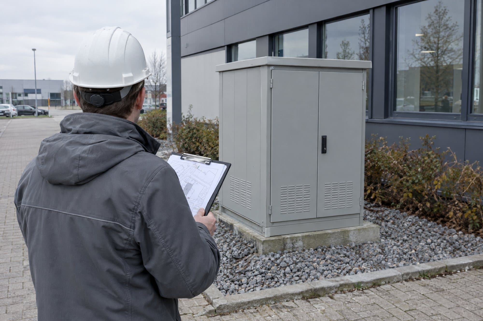 Engineer with a site plan in front of a distribution cabinet at a commercial building